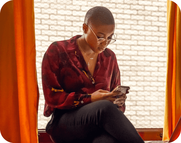 Woman sitting between orange curtains, hunched over looking at smart device