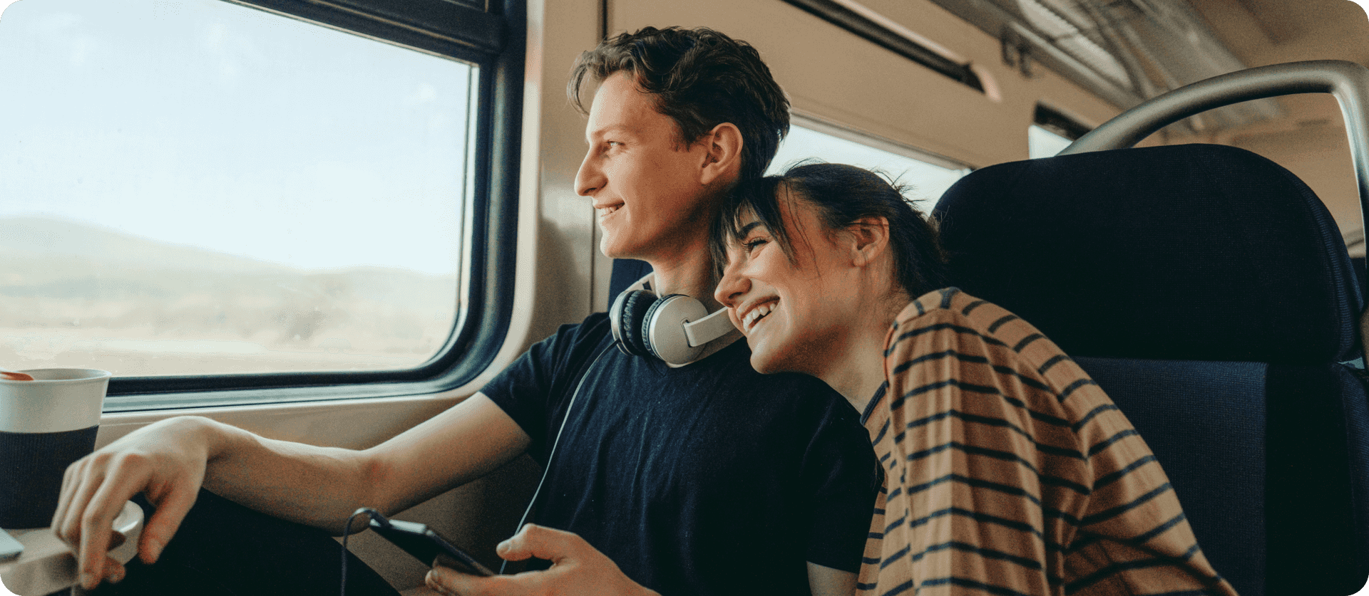 A man and woman sitting on a train smiling and staring out the window.