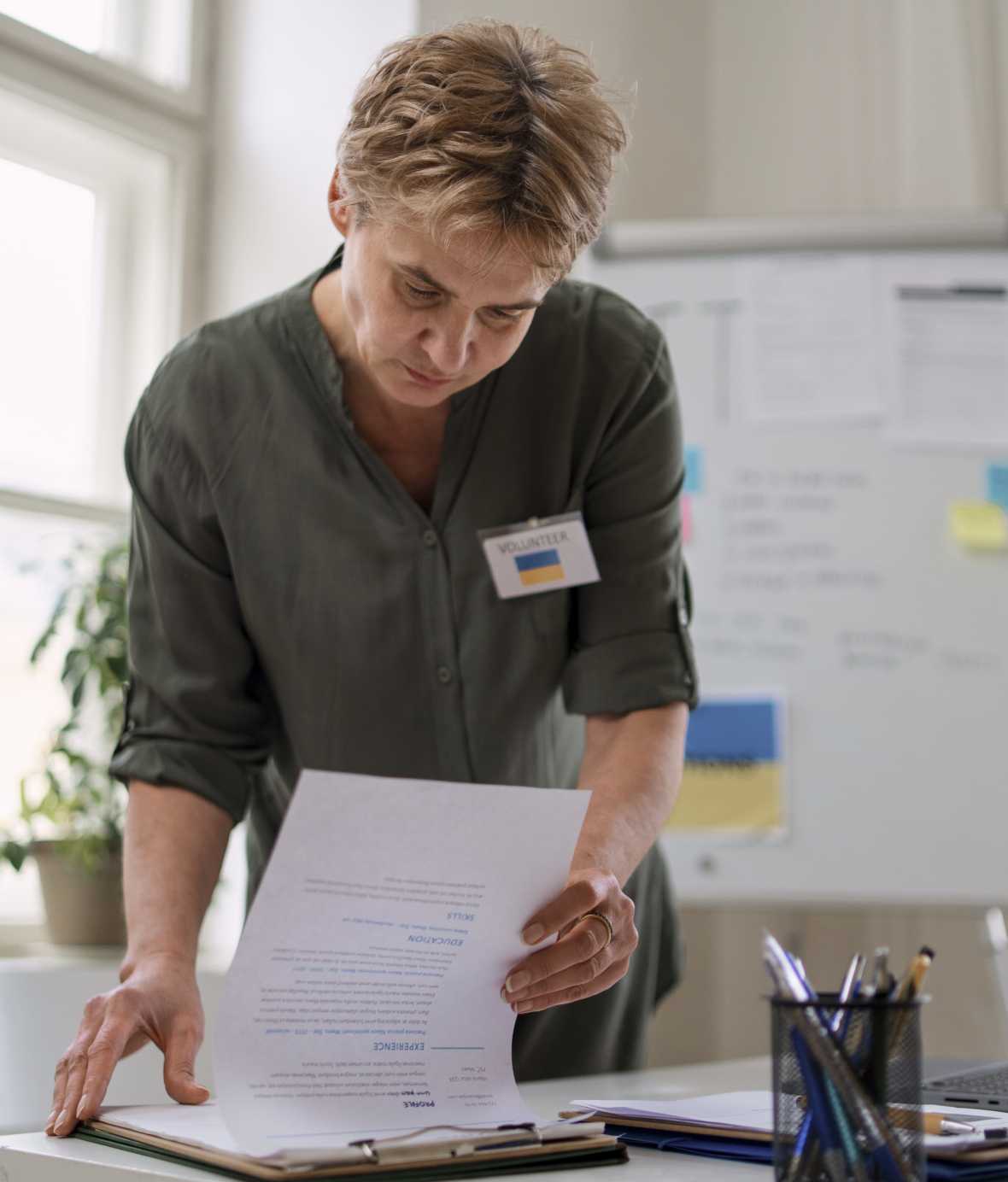 Woman in a classroom hunched over a table while looking at papers. 