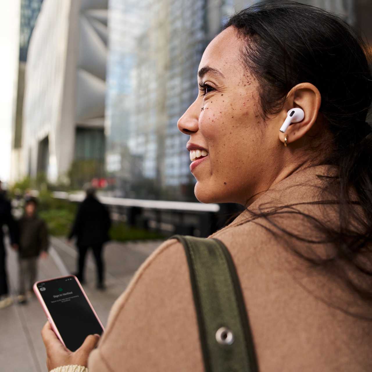 Woman walking on city street listening to airpods while using a smart device authenticated by Okta Verify