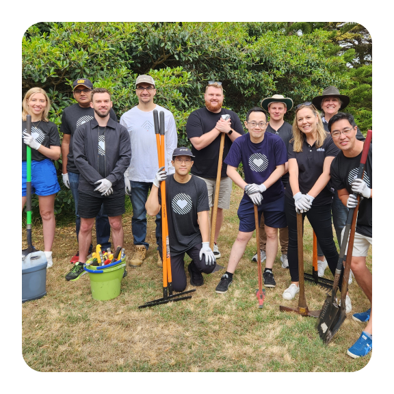 Image of Okta employees posing with rakes and shovels in a park