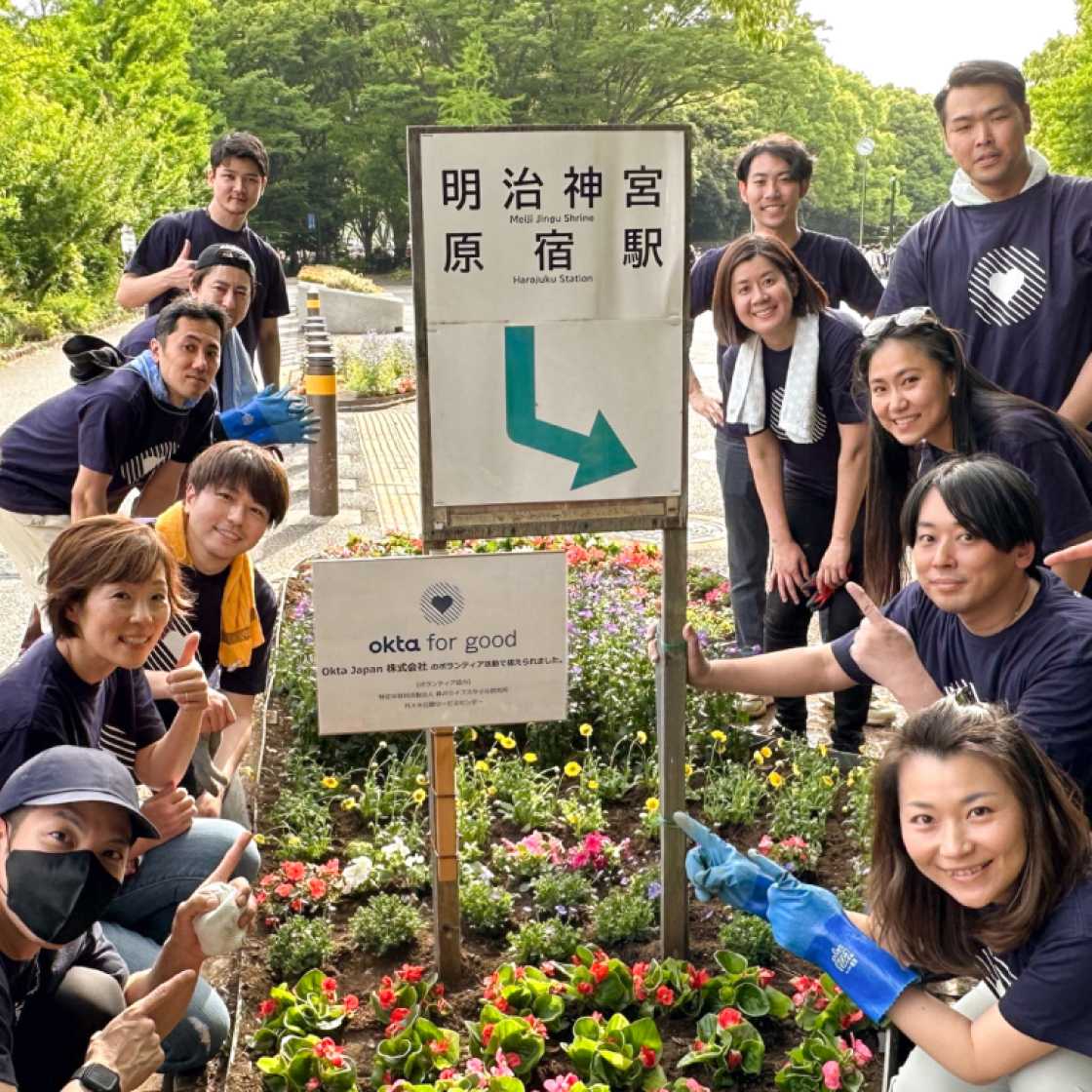 Group of volunteers in garden crowded around sign that says Okta for Good and another sign in Japanese