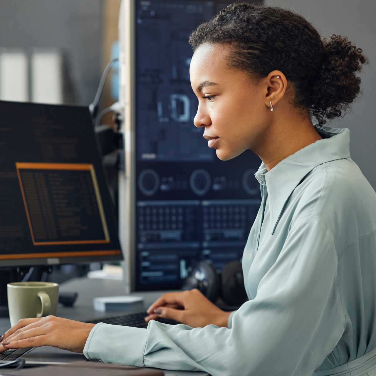 Woman sitting and working at a desktop computer with a coffee mug in front of her.