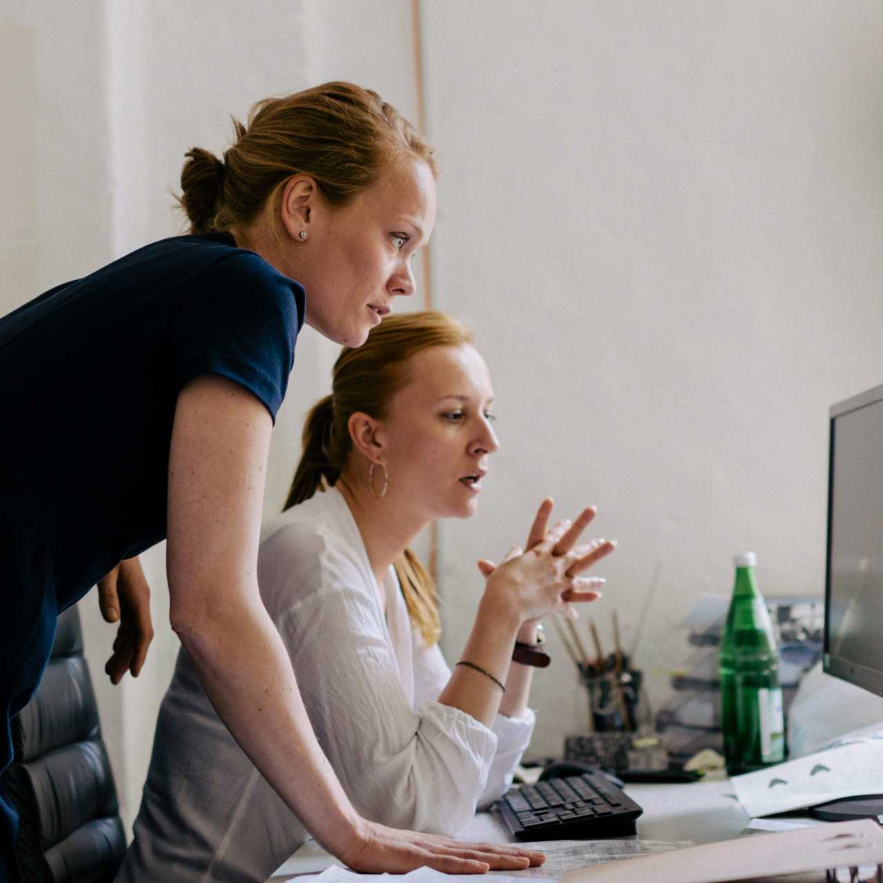 Two women at desk talking and looking at desktop computer