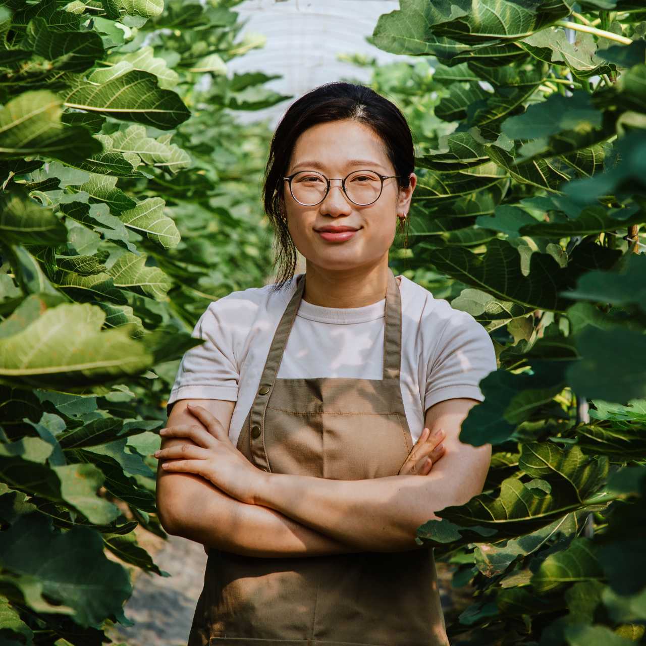 Woman with glasses and brown overalls in greenhouse posing for camera 