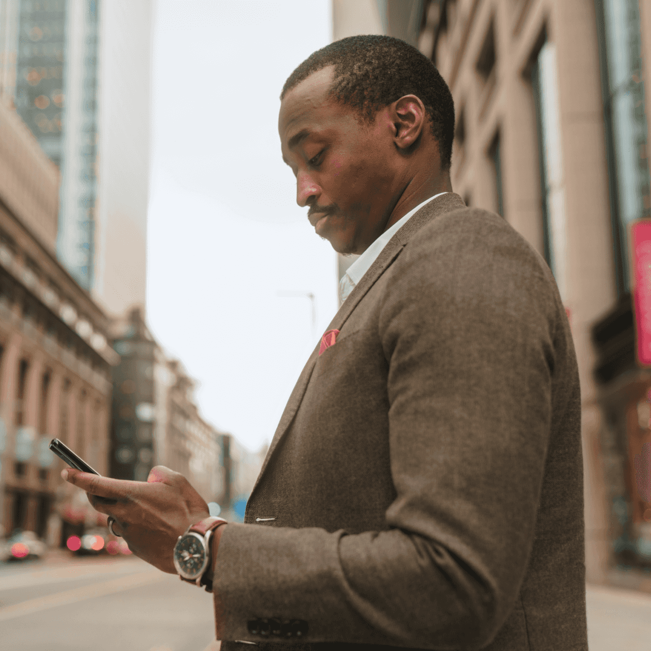 Image of man in a suit on city street looking at smart phone.