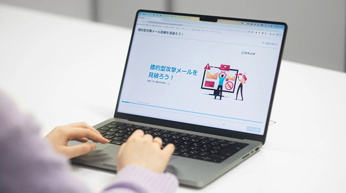 A male speaker wearing a dark blazer over a white shirt addresses an audience from behind a podium. He is captured in a medium shot against a dark blue and purple geometric backdrop.