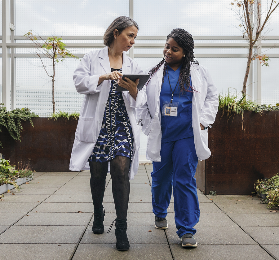  Two medical professionals walking and discussing data on a tablet to bridge on-prem, legacy, and cloud healthcare systems.