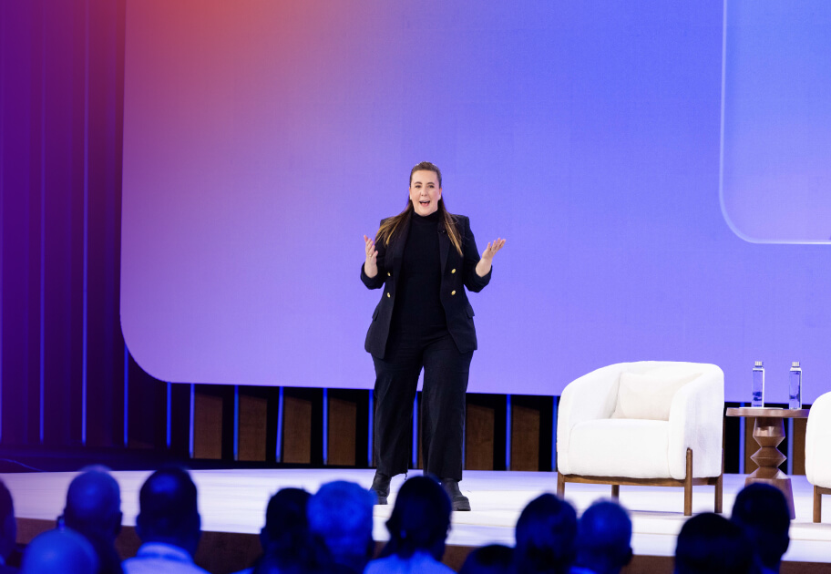 Leader at Okta speaks on stage at the Oktane conference. She is wearing a black blazer and standing in front of a large light purple screen.