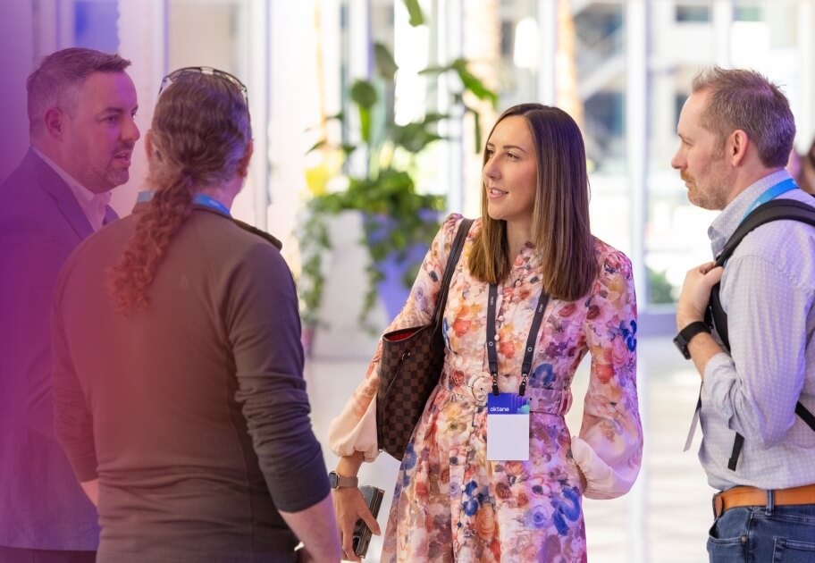 A group of Oktane attendees networking in a brightly lit conference hall.