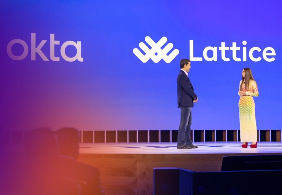  A man and a woman stand on stage at the Oktane conference. The screen behind them displays the Okta and Lattice logos.