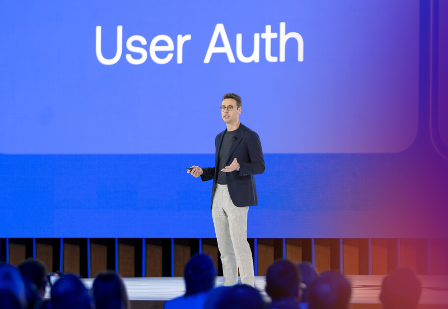 A man speaks on stage at the Oktane conference in front of a large blue screen that reads, "User Auth."