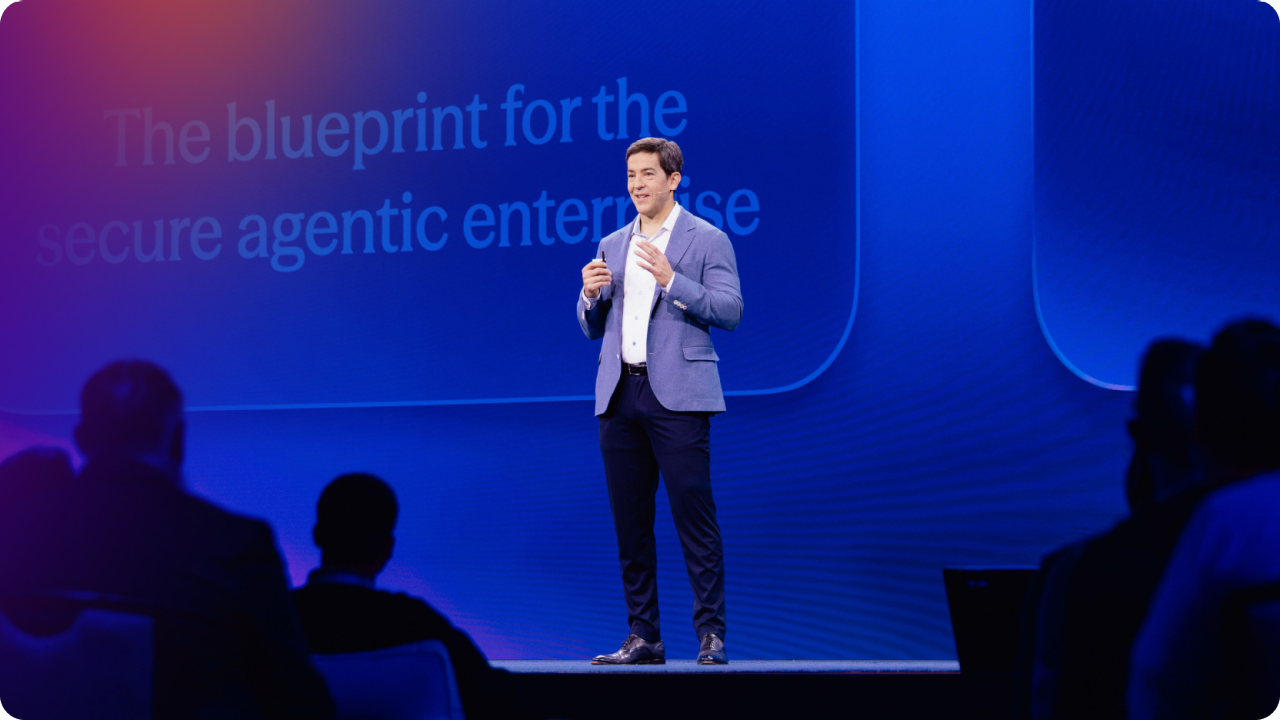 Okta CEO Todd McKinnon speaking on stage at Oktane presenting a keynote with a backdrop reading 'The blueprint for the secure agentic enterprise."
