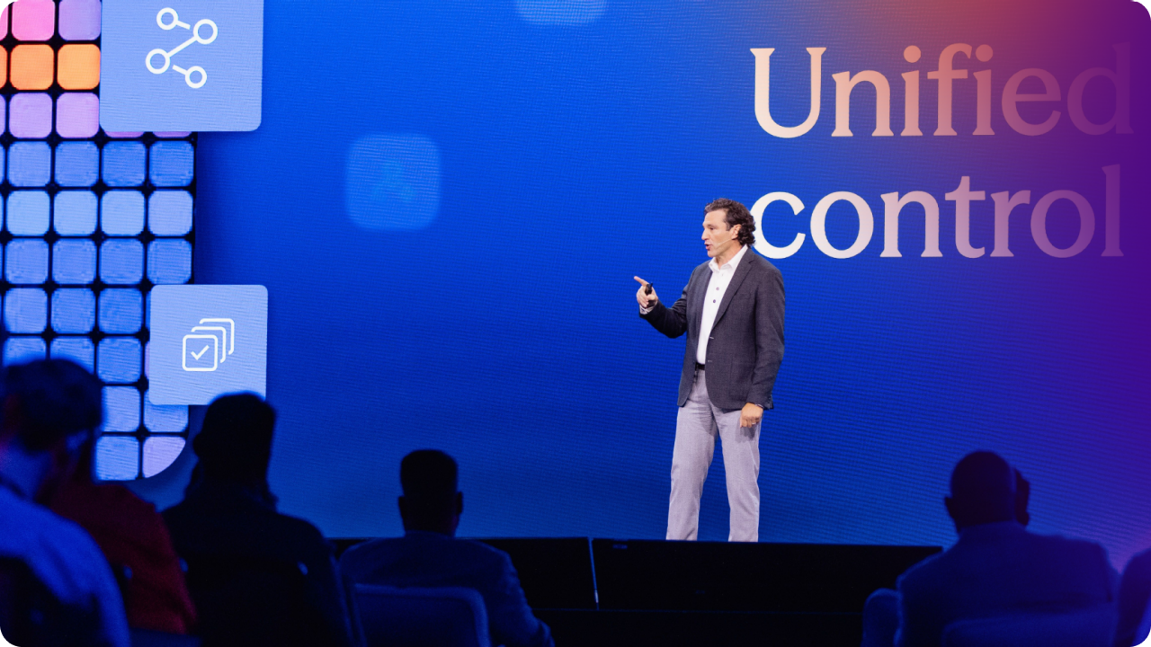 Harish Peri in a blue suit jacket standing on stage with arms outstretched.