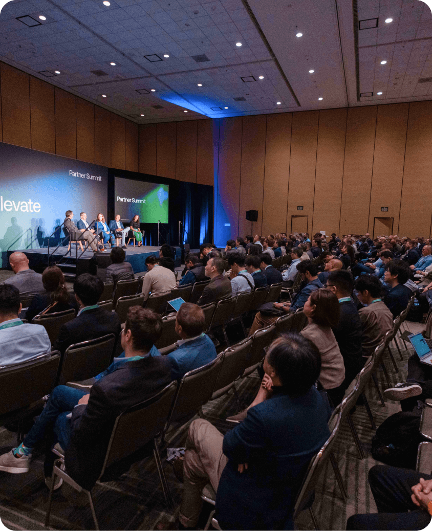 Partner Summit attendees sitting and watching speakers on stage.