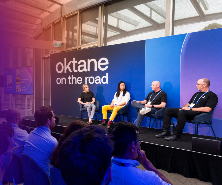 Four panelists seated on a stage in front of a blue backdrop with the text "Oktane on the road" speaking to an audience.