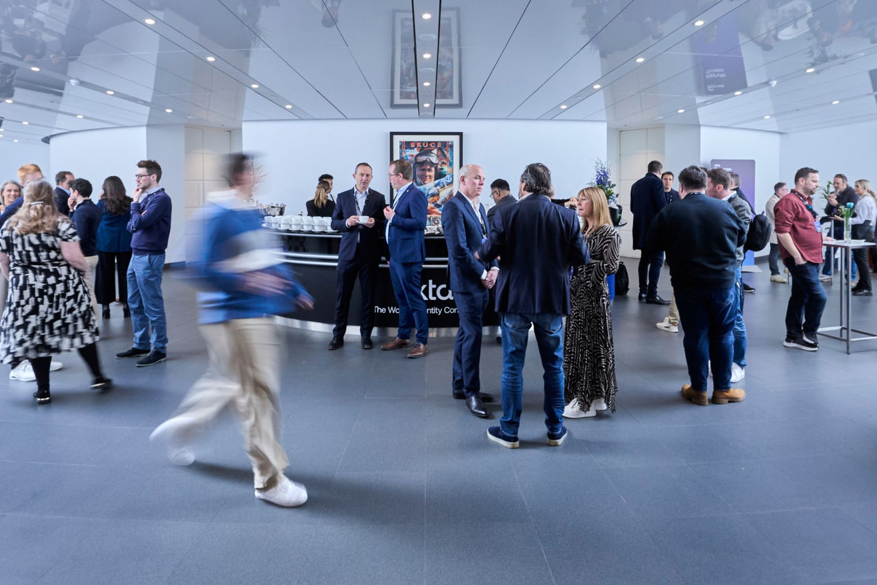 A wide shot of event attendees networking and conversing in the modern, branded lobby during the Okta Showcase event.