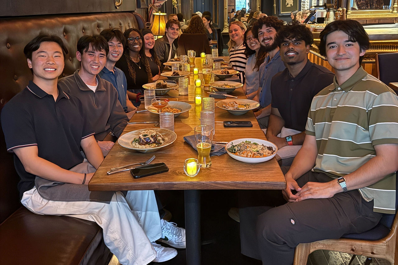 A group of individuals seated at a wooden table in a warmly lit restaurant setting. 