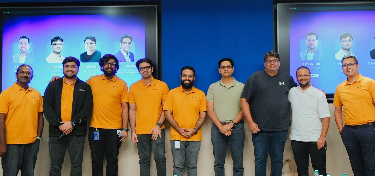 A group of people stands in a row posing for a team photo in front of a large presentation screen. 