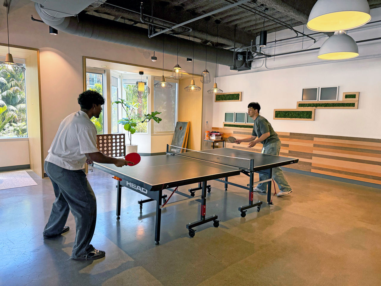 Two men are engaged in a game of table tennis in a modern indoor setting. 