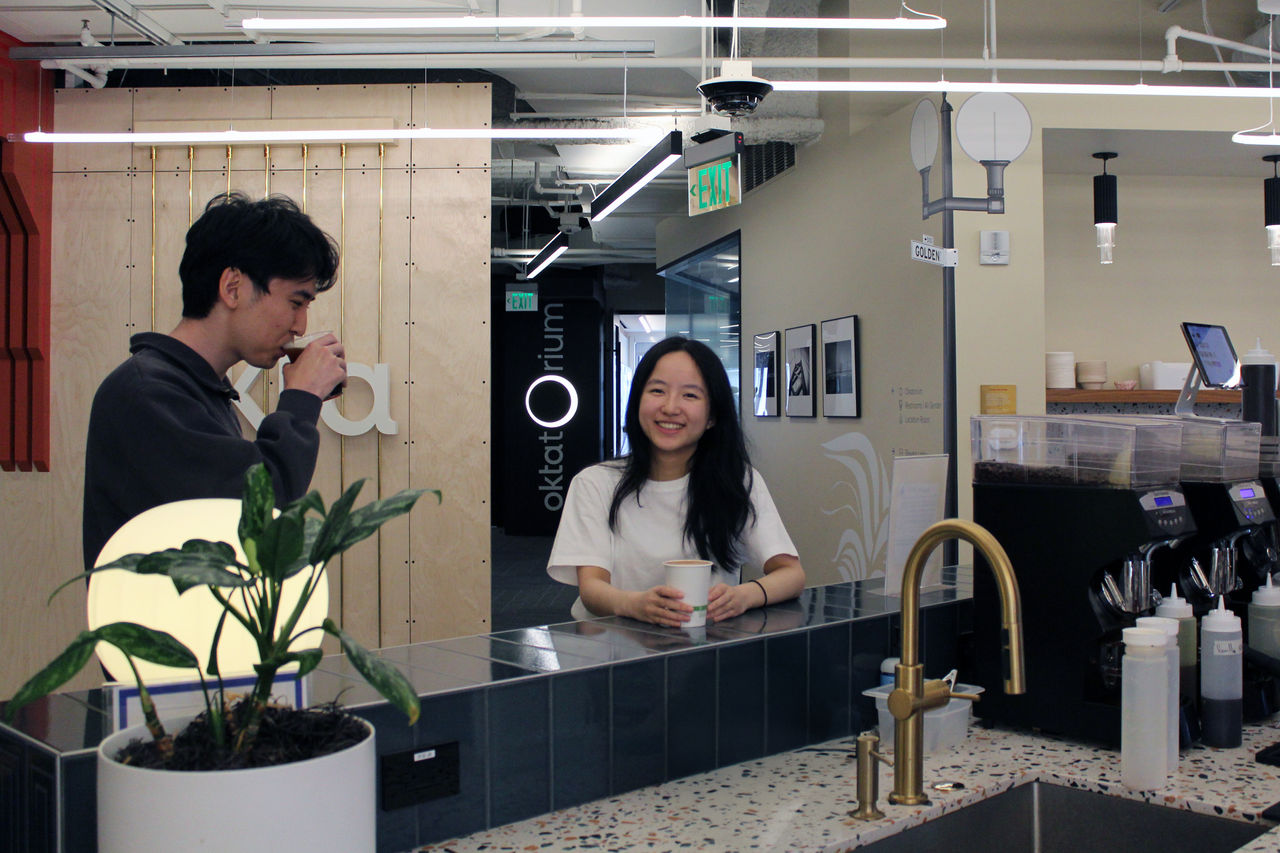 A sleek coffee counter with a terrazzo countertop and gold faucet is set in a contemporary office environment.